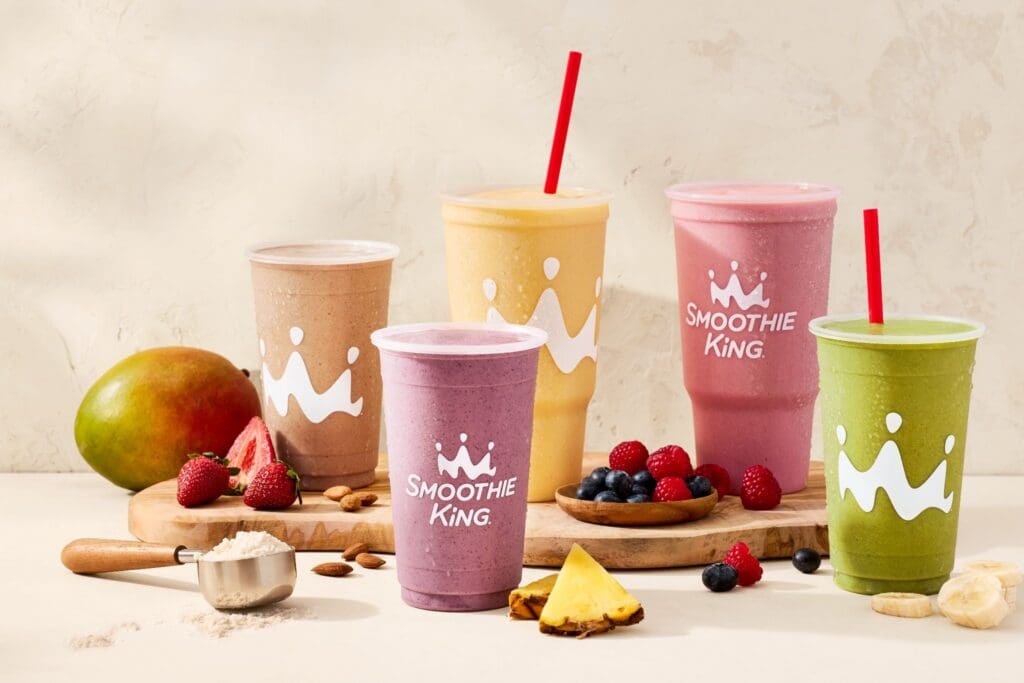 A lineup of Smoothie King Smoothie's on a table with fruit.