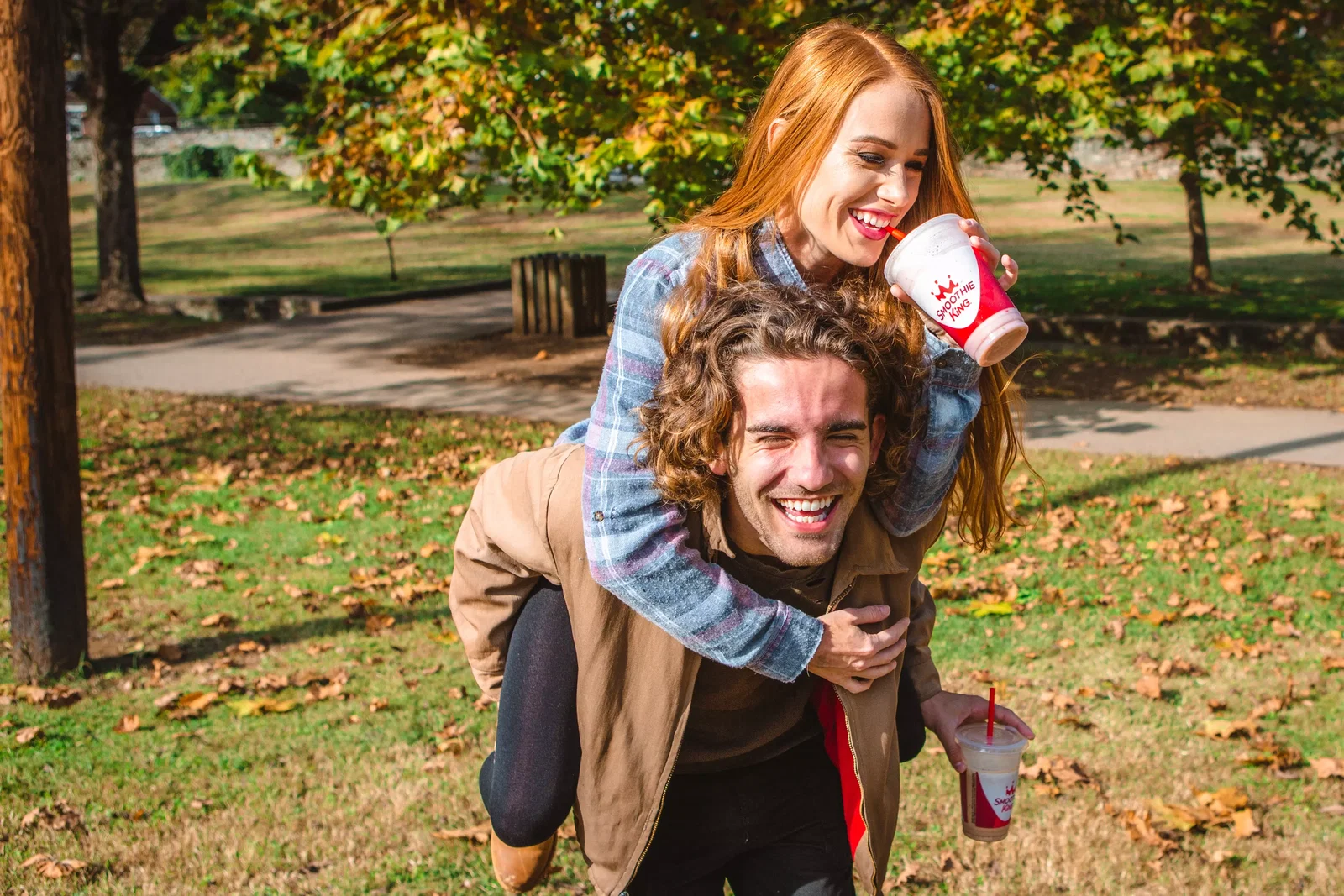A guy giving a girl a piggyback ride as they both drink the best fruit smoothies from Smoothie King