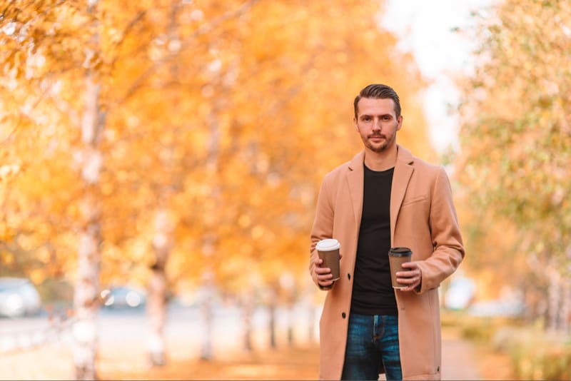 Man holding coffees with fall trees in the background