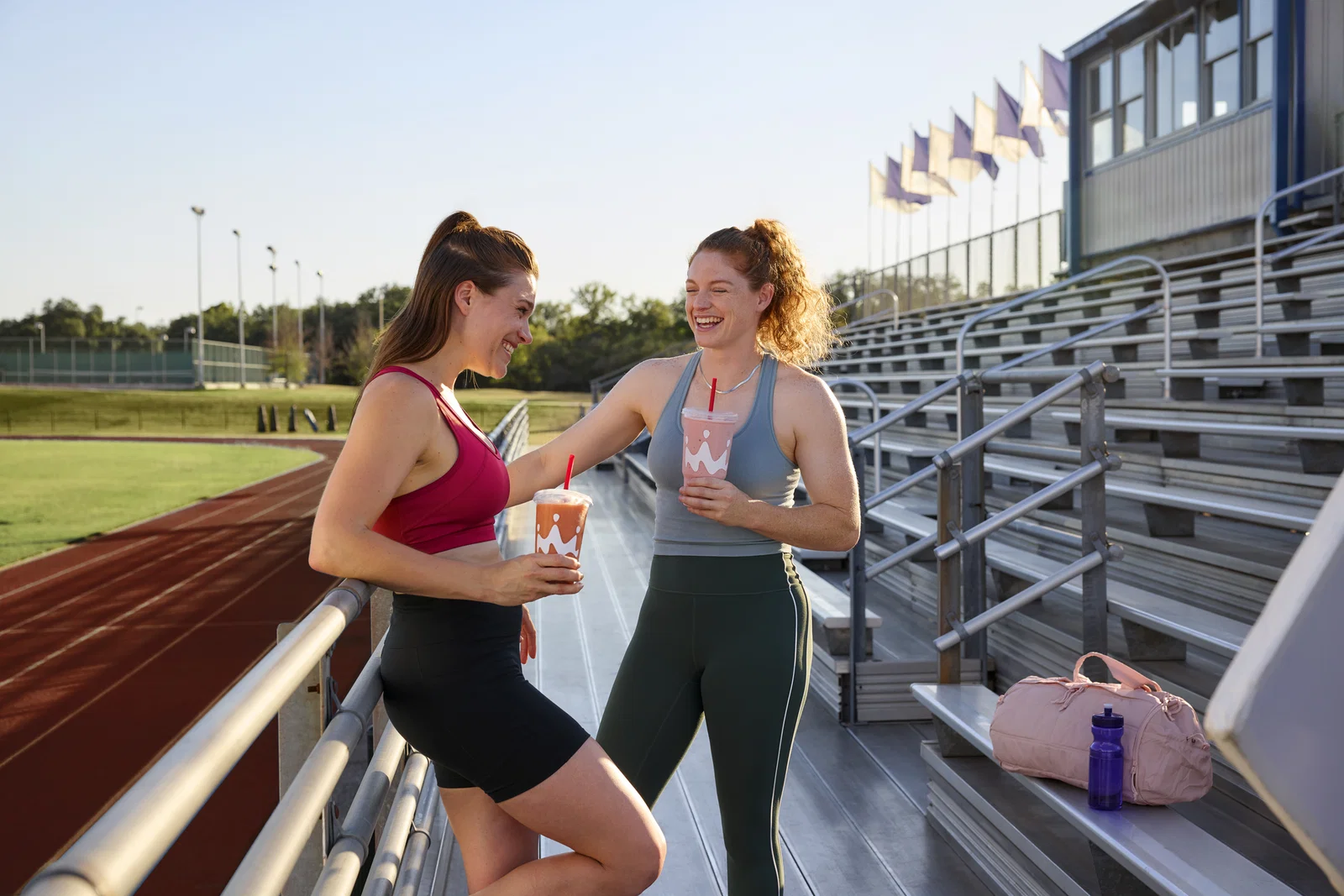 Two women drinking Smoothie King hydration smoothies after a run on a track